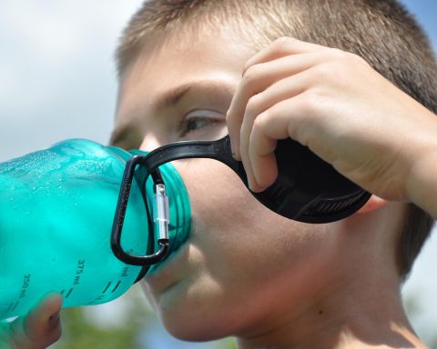 Persoon drinkt een glas water op een zonnige zomerdag buiten