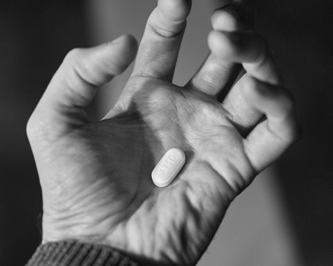 Een hand houdt witte antibioticapillen vast naast een glas water