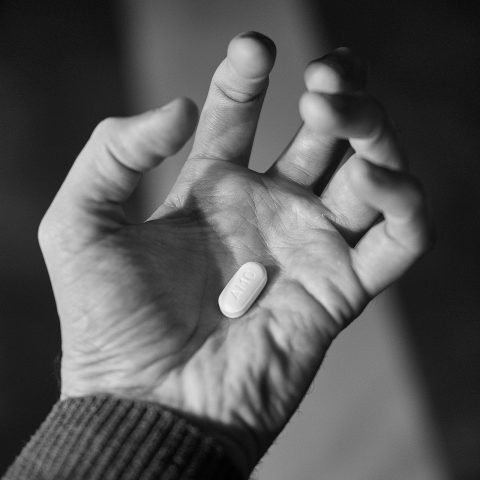 Een hand houdt witte antibioticapillen vast naast een glas water